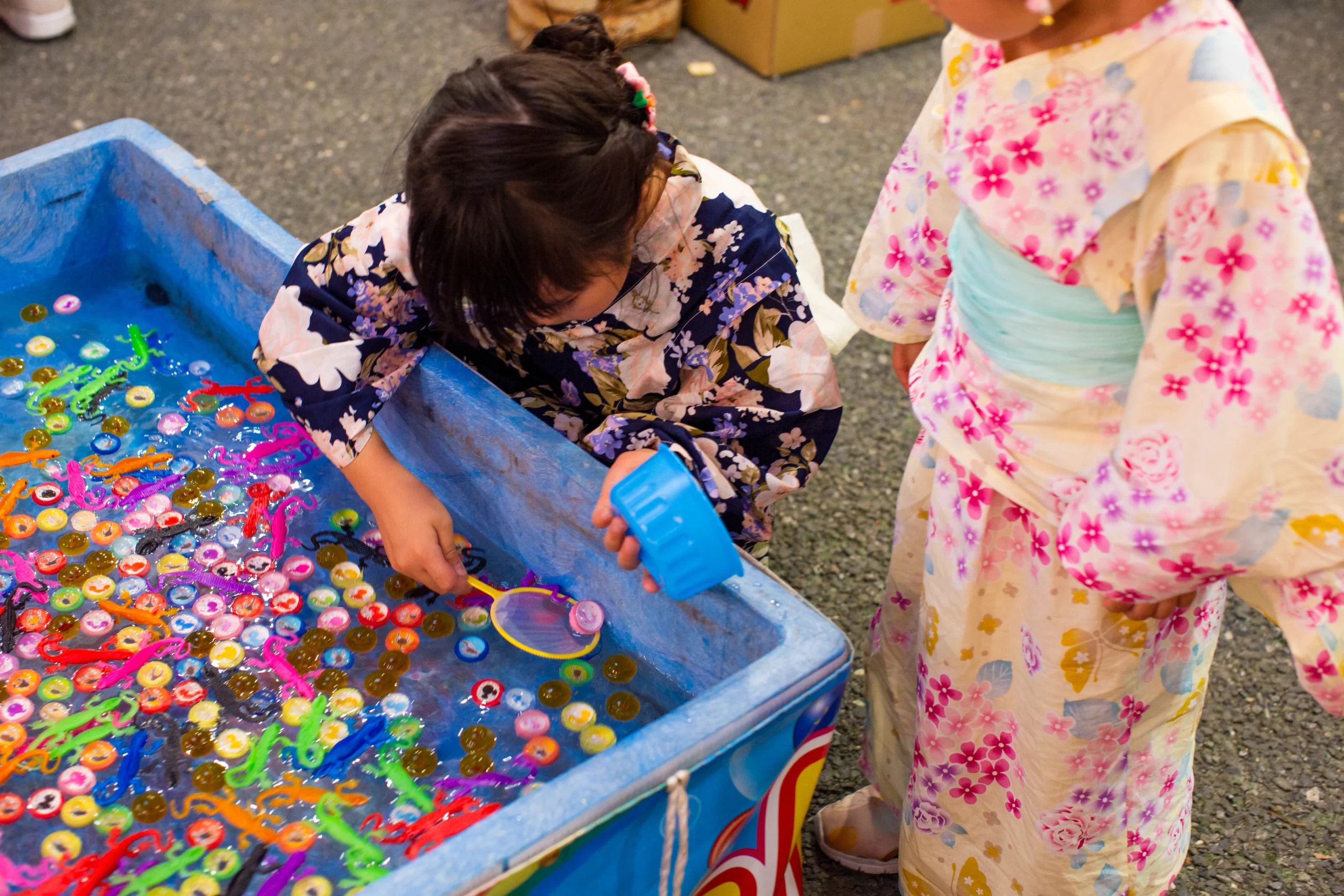 浴衣を着た子供たちが縁日の水槽ゲームで遊ぶ様子